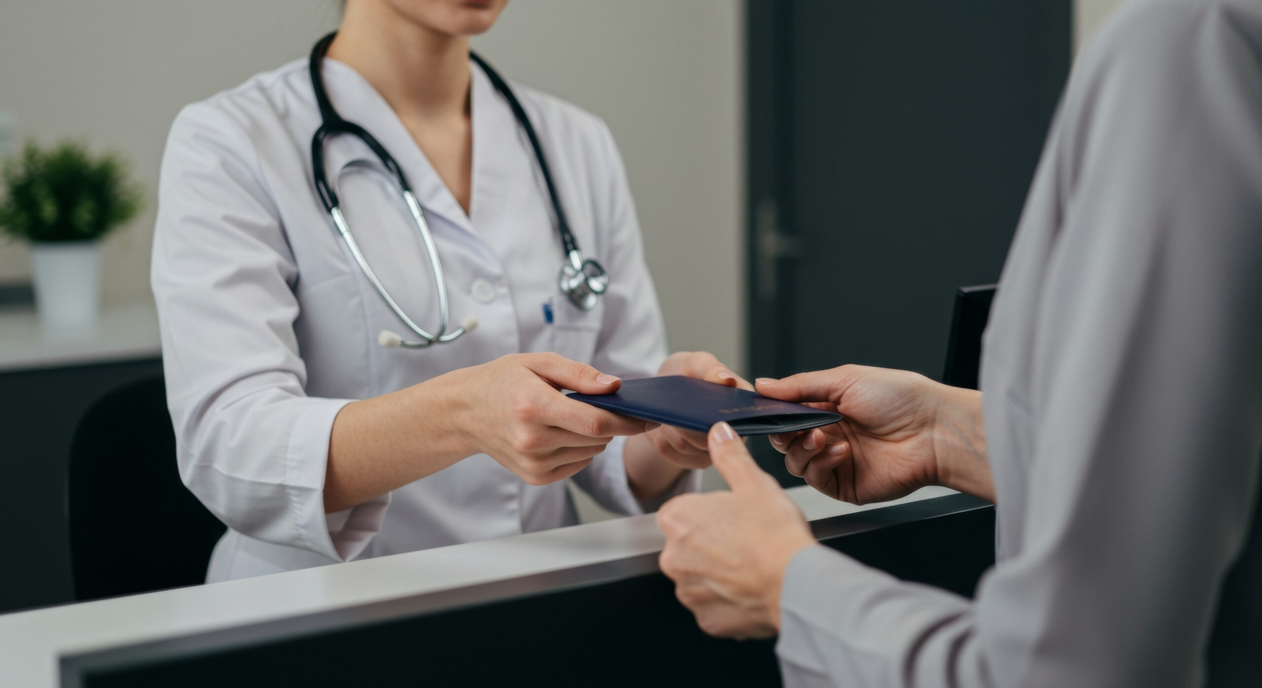 A female doctor in a white uniform transfers a dark blue passport to a patient at a clinic reception desk.