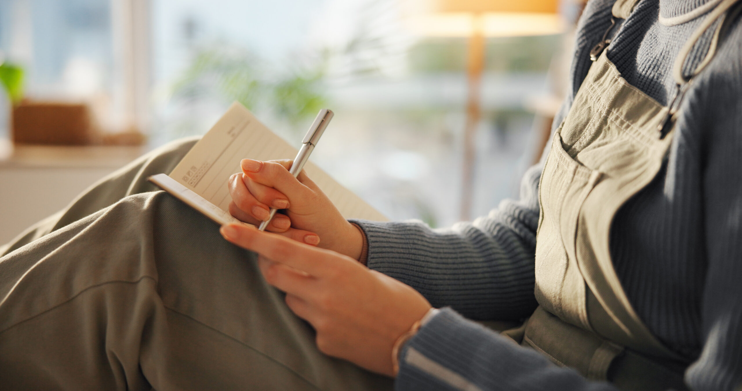 Hands, person or writing in notebook in home for journal entry, schedule reminder or calendar tasks. Personal diary, woman and taking notes in apartment for to do list, inspiration and agenda planner.