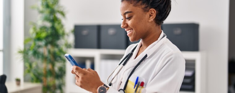 African american woman wearing doctor uniform using smartphone working at clinic