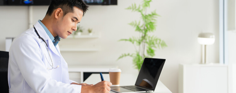 Doctor looking at laptop screen writing in notebook for research planning or medical tech innovation in hospital office. Healthcare medic worker, research strategy book notes and online communication.