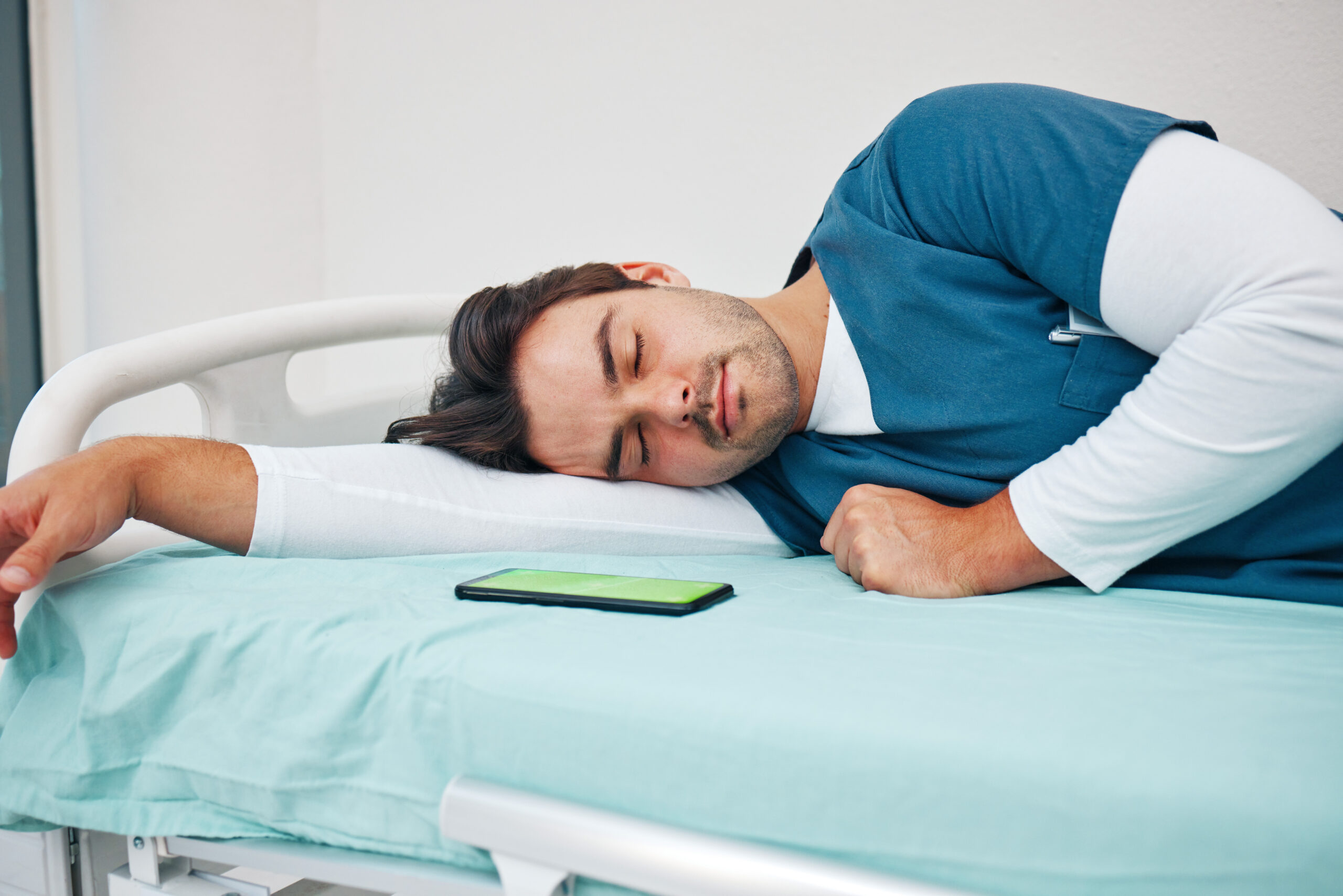 Sleeping, hospital and tired doctor with phone on bed for rest, nap and break for burnout, exhausted and fatigue. Healthcare, night shift and worker relax for medical service, wellness and stress.