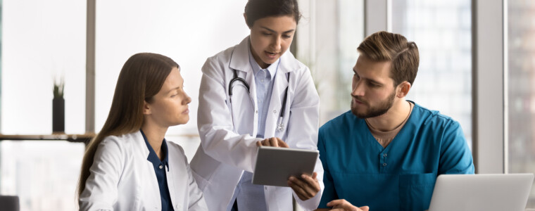 Mentorship in healthcare. Smiling young woman doctor mentor supervisor teach diverse couple interns explain mentees diagnosis using patient health data electronic xray image on digital tablet screen