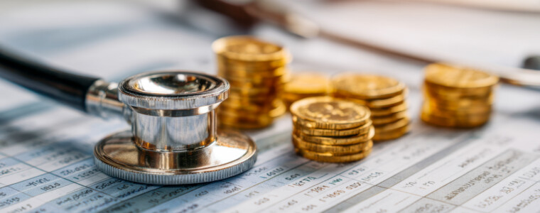 Medical stethoscope placed on financial documents alongside stacks of gold coins symbolizing healthcare costs and economic considerations in medicine