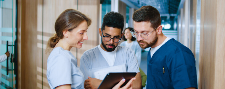 Side view portrait of multicultural group of young medical professionals chatting during break in contemporary hospital corridor. Nurses and doctors using gadgets online.
