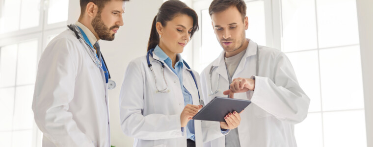 Three doctors in medical office reviewing test results on tablet and discussing treatment plan.